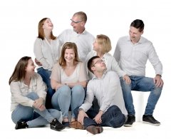 Familie zittend op de grond lachend naar elkaar met achtergrond wit met 7 personen gefotografeerd in fotostudio Rotterdam. www.marijnissenfotografie.nl