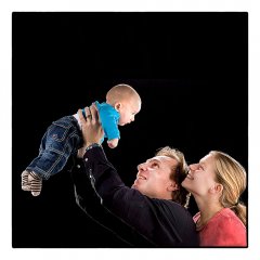 Gezin met baby waarvan de vader de baby in de lucht houdt alsof het vliegt de ouders kijken verliefd naar hun kind en de baby kijkt naar hun gefotografeerd in de fotostudio Marijnissen Fotografie Rotterdam.