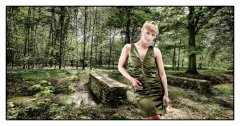 Foto gemaakt in greenscreen fotostudio fotomodel staat voor een honderden jaren oud bruggetje in het bos ze kijkt recht in de camera en haar jurk heeft dezelfde kleur als haar omgeving gefotografeerd door fotograaf fotostudio Marijnissen Fotografie Rotterdam.