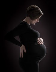 Zwangerschapsshoot met zwart jurkje en zwarte achtergrond stijlvol verlicht waardoor de zwangerschapsbuik goed uitkomt op de foto, gefotografeerd in fotostudio Rotterdam. www.marijnissenfotografie.nl