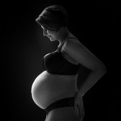 Zwangerschap foto stijlvol in mooie zwarte lingerie met zwarte achtergrond sfeervol verlicht waardoor de zwangerschapsbuik goed uitkomt gefotografeerd in fotostudio Rotterdam. www.marijnissenfotografie.nl