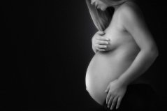 En profiel zwangerschap foto met blote buik en hand op borst met zwarte achtergrond in zwart-wit gefotografeerd in fotostudio Rotterdam. www.marijnissenfotografie.nl